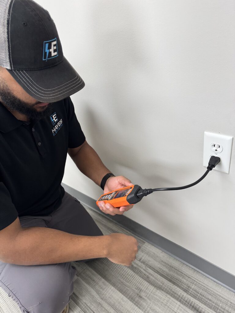 A Hayes Electrical technician performs diagnostics on an electrical outlet with a specialized tester.