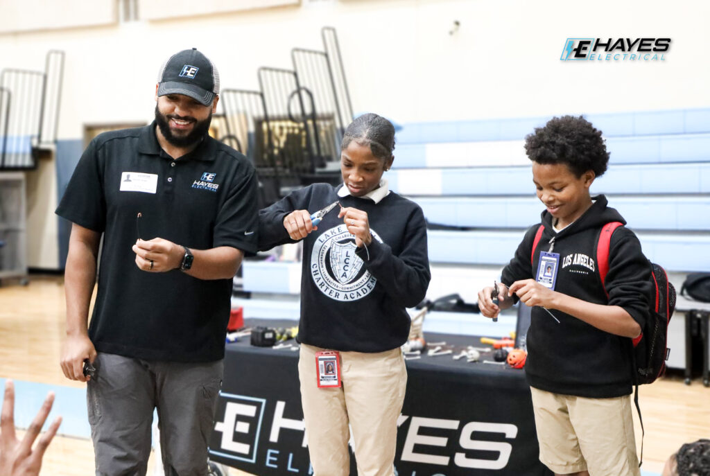 Hayes Electrical team members engage with students, demonstrating basic electrical skills and tools at a community event.